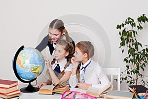 Three girls in the school geography lesson learn globe knowledge