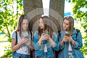Three girls schoolgirl teen. In summer park by tree. He holds a smartphone in his hands, writes messages, reads