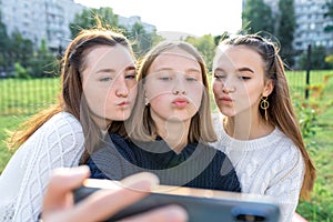 Three girls schoolgirls teenagers summer city. Photography on phone, selfie photo, online app smartphone, social