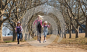 Three girls sisters running skipping down tree lined dirt road