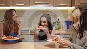 Three girls are sitting at the kitchen table and taking their plates of food in their hands, smelling the aroma of