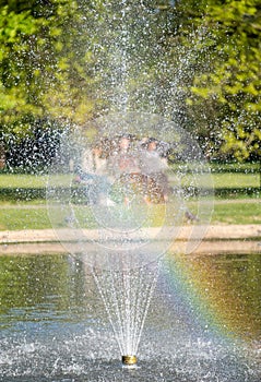 Three girls sitting on park bench at Pinner Memorial Park, Middlesex UK. Photographed through the fountain at the duck pond. photo