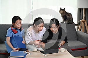 Three girls sitting on sofa and playing games online with  with computer tablet in living room.