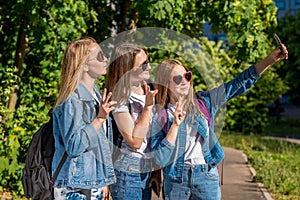 Three girls are teenage girlfriends. In summer after school, in the park. Photographs on a smartphone. Wear jeans