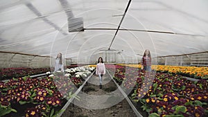 Three girls walks synchronously to camera among flower seedlings