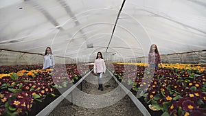 Three girls walks synchronously to camera among flower seedlings