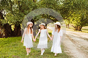 Three girls in white dresses walk in nature in the summer. Children`s pastime during the summer holidays.