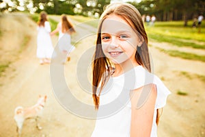 Three girls in white dresses walk in nature in the summer. Children`s pastime during the summer holidays.