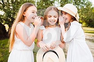 Three girls in white dresses walk in nature in the summer. Children`s pastime during the summer holidays.