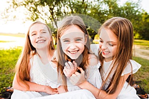 Three girls in white dresses walk in nature in the summer. Children`s pastime during the summer holidays.