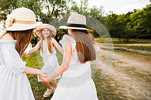 Three girls in white dresses walk in nature in the summer. Children`s pastime during the summer holidays.