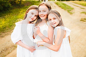 Three girls in white dresses walk in nature in the summer. Children`s pastime during the summer holidays.