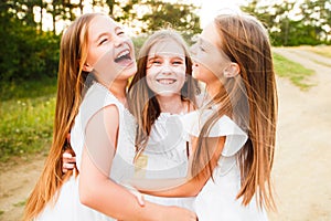 Three girls in white dresses walk in nature in the summer. Children`s pastime during the summer holidays.