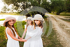 Three girls in white dresses walk in nature in the summer. Children`s pastime during the summer holidays.