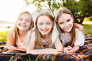 Three girls in white dresses walk in nature in the summer. Children`s pastime during the summer holidays.