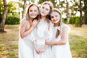 Three girls in white dresses walk in nature in the summer. Children`s pastime during the summer holidays.