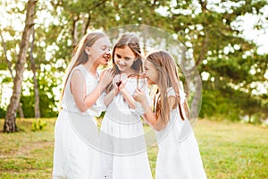 Three girls in white dresses walk in nature in the summer. Children`s pastime during the summer holidays.