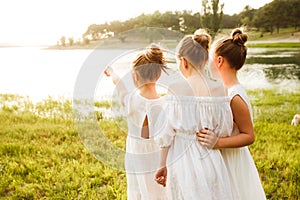 Three girls in white dresses walk in nature in the summer. Children`s pastime during the summer holidays.