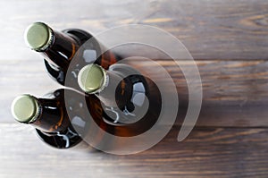 Three glass bottles of dark beer stand on a brown wooden background. The view from the top. Copy space