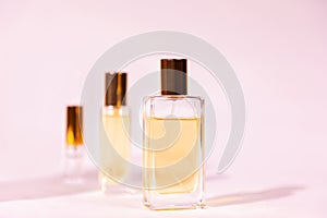 Three glass bottles of golden perfume on pink background. Copy space