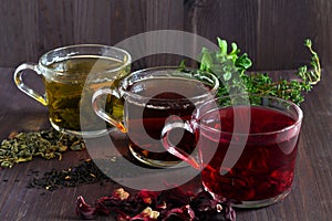 Three glass cups with black, red and green tea on a dark wooden background.