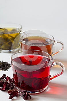 Three glass cups with black, red and green tea on a white background.