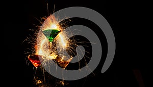 Three glass cups of cocktail with sparks reflecting in glass with a black background