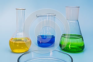 Three glass laboratory flasks with solutions of yellow, green and blue on a gentle blue medical background. The concept of medical