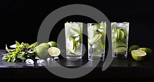 Three glasses of cocktail mojito lemonade on the bar. Party cocktail. Lime, ice and mint on the table. Black background.