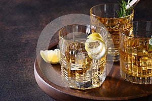 Three glasses of cold whiskey served on rocks with rosemary, lemon peels on brown. Copy space.