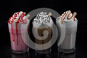 Three glasses of colorful milkshake cocktails - chocolate, strawberry and vanilla, isolated at black background