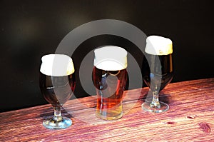 Three glasses of different types of dark beer are in a row on a wooden table