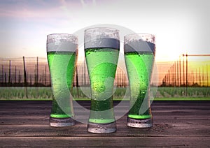 Three glasses of green beer with hop-garden background - 3D render