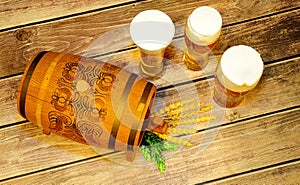Three glasses of light beer with foam, a wooden barrel, hops and ears of corn on a wooden table