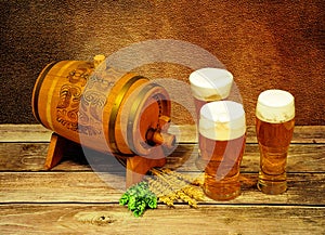 Three glasses of light beer, a wooden barrel, wheat ears and hops on a wooden table
