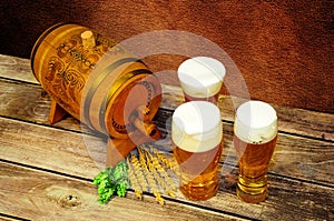 Three glasses of light beer, a wooden keg, hops and malt on a wooden table