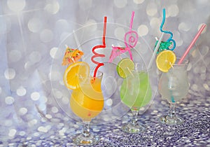 Three glasses with orange, lemon and lime citrus juices with ice and decorated with tubes and pieces of fruit stand in a row on a