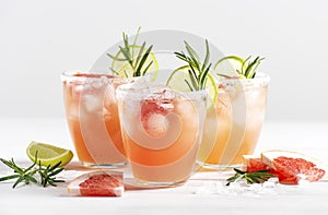Three glasses of paloma cocktail with ice and tequila, decorated with lime wedges, grapefruit and rosemary