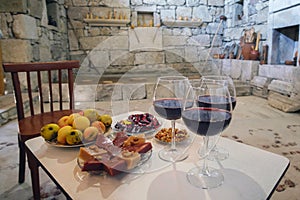 Three glasses of red wine on the table with traditional Georgian sweets pelamushi and friuts in marani