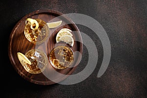 Three glasses of whiskey served on rocks with lemon on brown background. Copy space.