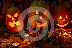 Three glowing pumpkins on halloween night with candles on a background of firewood and autumn foliage