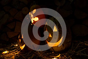 Three glowing pumpkins on halloween night with candles on a background of firewood and autumn foliage