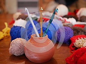 Three gold, green and white crochet hooks in a ceramic vase against a background of several multicolored balls of woolen thread on