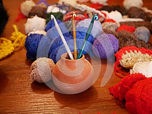 Three gold, green and white crochet hooks in a ceramic vase against a background of several multicolored balls of woolen thread on