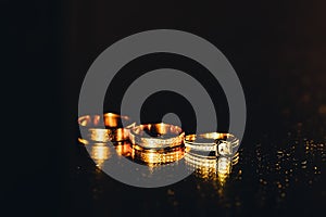 Three gold rings lie next to each other on a mirror background, wedding accessories on a black background