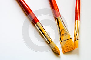 Three golden bristle paint brushes on white background with copy space