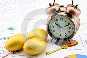 Three golden eggs and a golden key with a clock on business and financial reports.