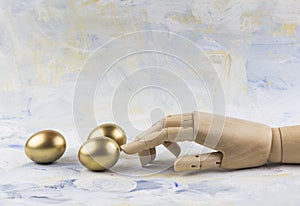 Three golden eggs touched by wooden puppet finger against painted clouds photo