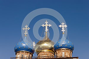 Three golden orthodox bright crosses are on top of blue and golden cupolas on the top of the stone church against blue dark sky