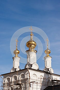 Three golden orthodox bright crosses are on top of golden cupolas on the top of the stone white under construction church against